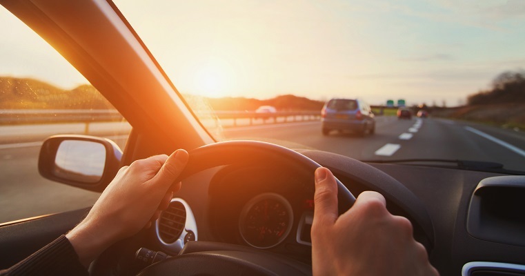 Hands on steering wheel. View of highway through windshield 