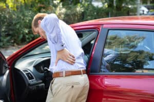 A man standing next to his car holding his lower back after an injury
