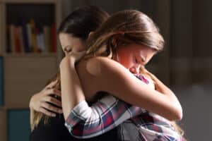 Grieving mother and daughter hug each other tightly following the death of a loved one. They are entitled to a financial settlement to secure their future without the father