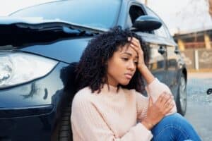 A woman sitting next to her car after a defective vehicle accident