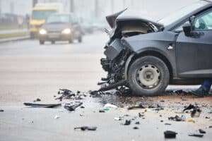 Black car with severe front-end damage after a traffic collision.