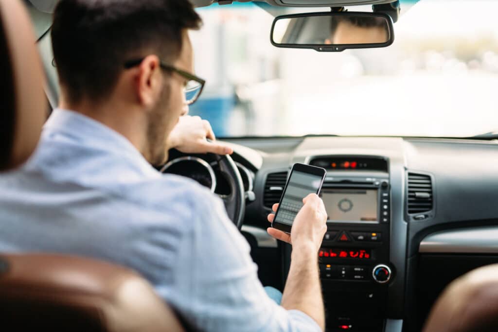 Driver using a smartphone behind the wheel, illustrating distracted driving and cell phone use while driving.